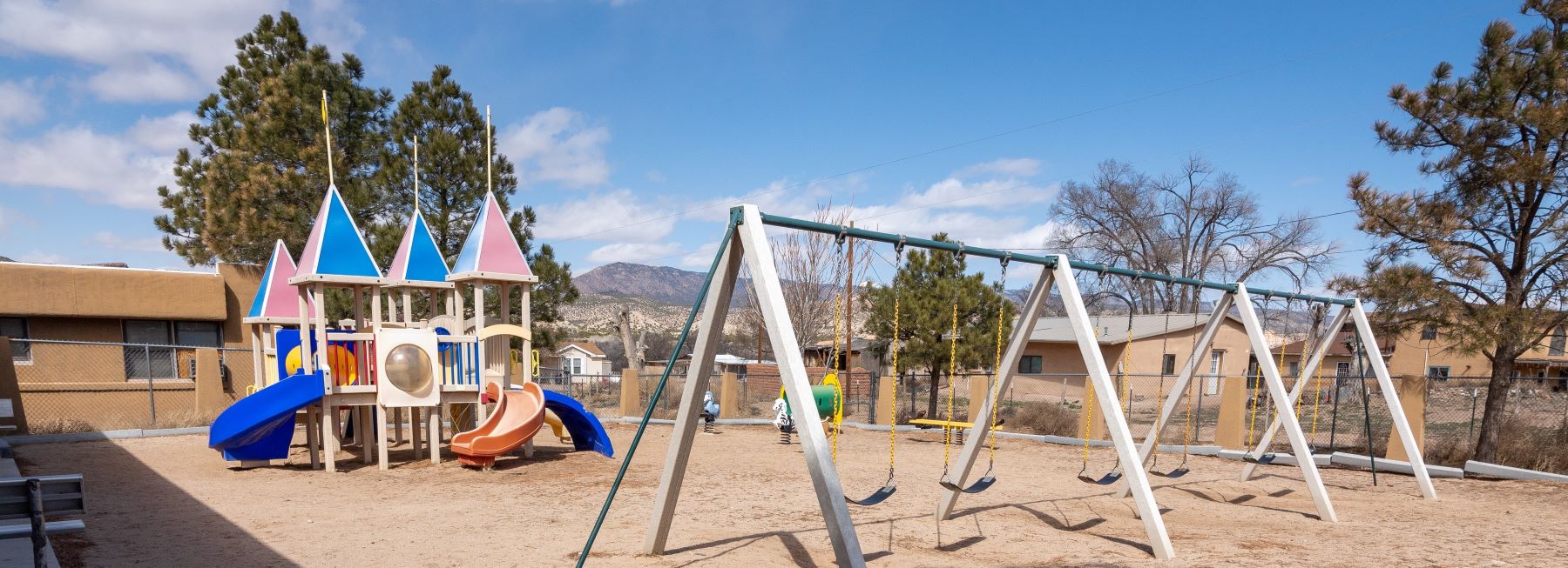 A playground featuring swings and slides set against a backdrop of a vast desert landscape under a clear blue sky.